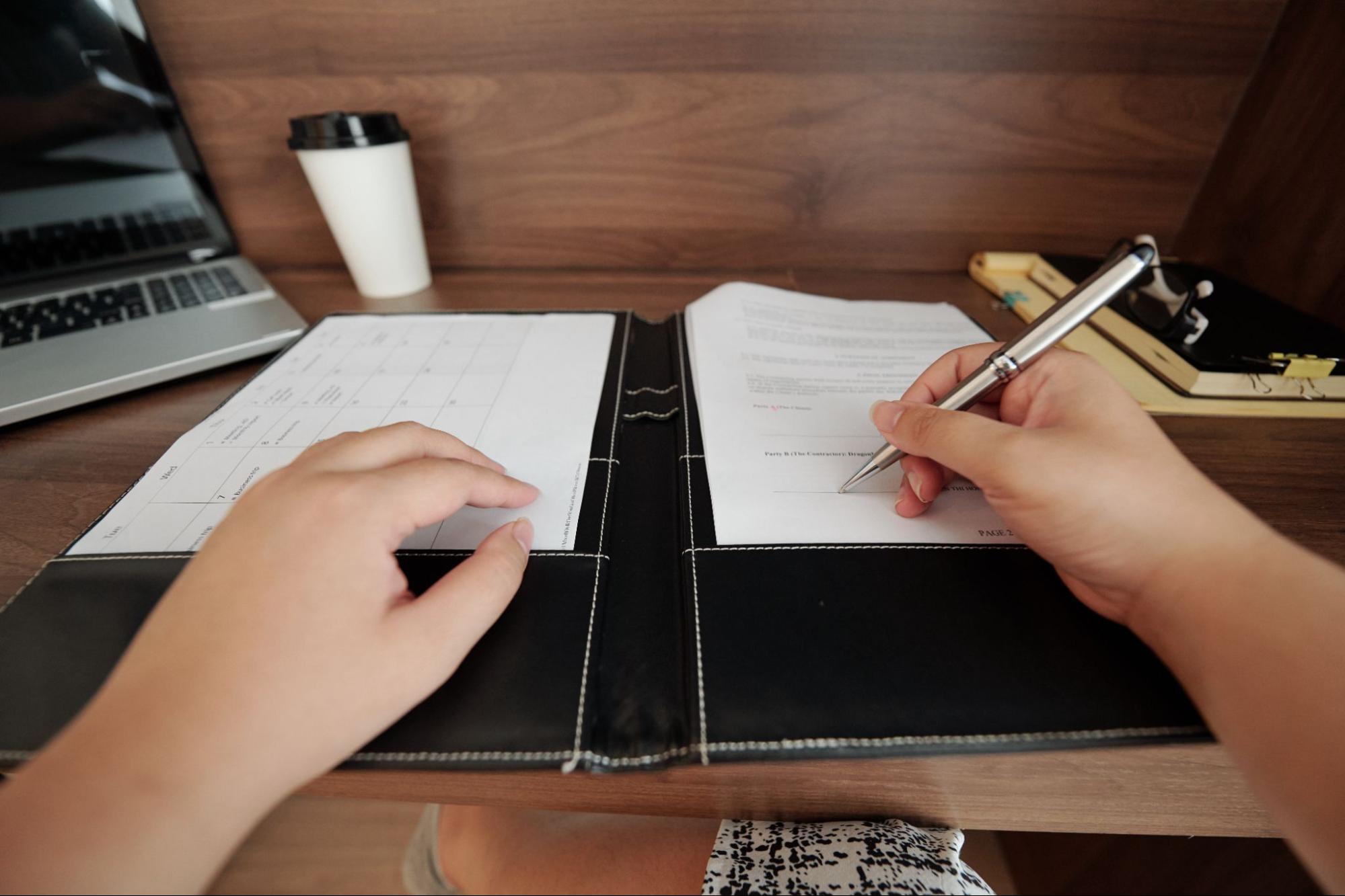 Person signing estate planning documents with a laptop in the background